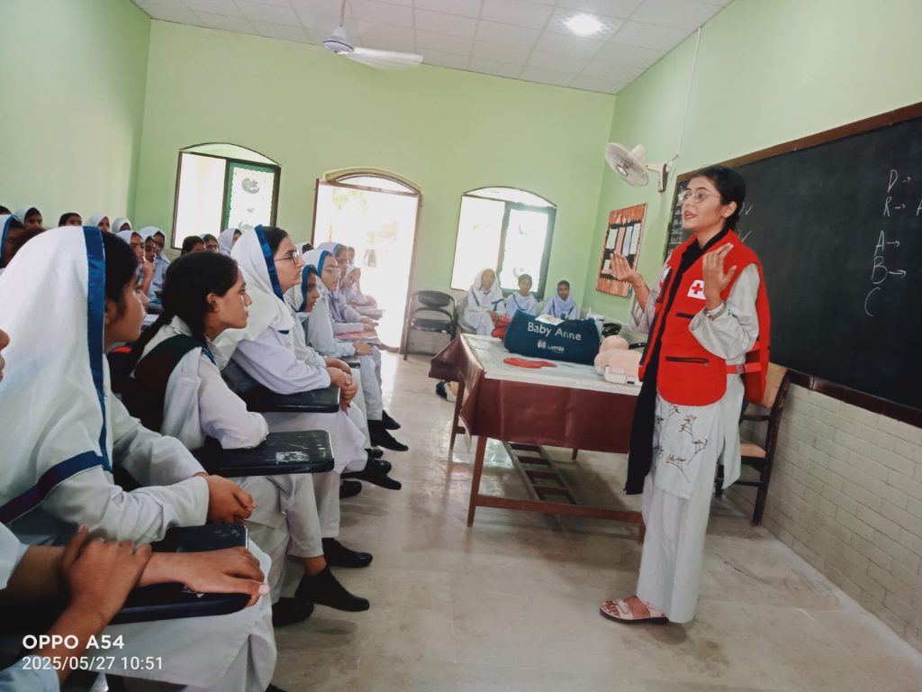 Several school children seated on the floor in a room, participating in a group learning first Aid session.