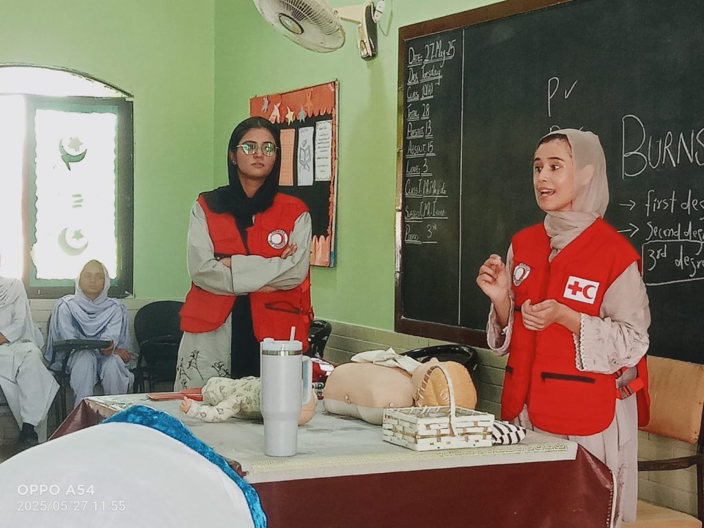Several school children seated on the floor in a room, participating in a group learning first Aid session.