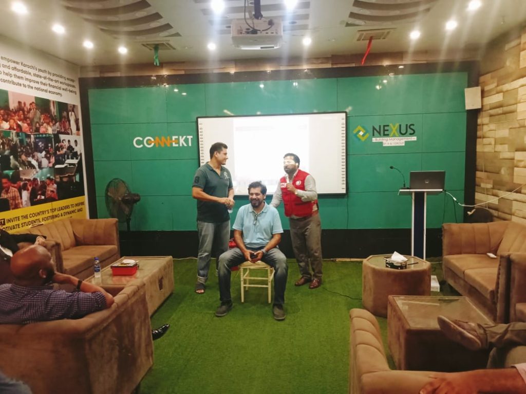 A man in a red Jacket stands in front of a screen, presenting first aid techniques at RJ Mall's orientation session