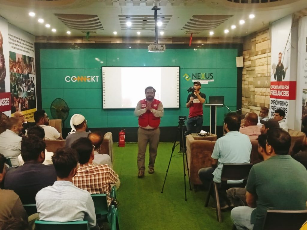 A man in a red Jacket stands in front of a screen, presenting first aid techniques at RJ Mall's orientation session