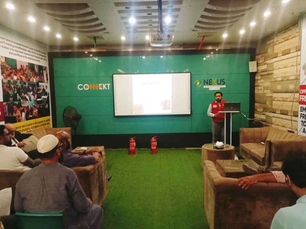 A man in a red Jacket stands in front of a screen, presenting first aid techniques at RJ Mall's orientation session