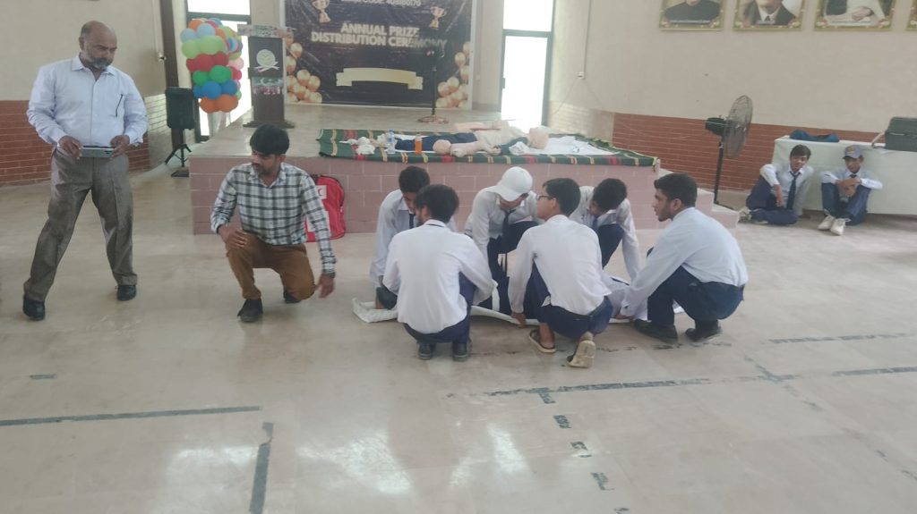 Several school children seated on the floor in a room, participating in a group learning first Aid session.