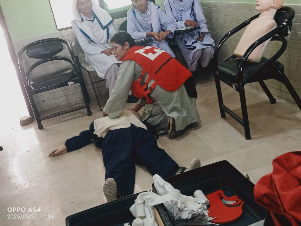Several school children seated on the floor in a room, participating in a group learning first Aid session.