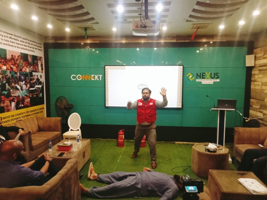 A man in a red Jacket stands in front of a screen, presenting first aid techniques at RJ Mall's orientation session