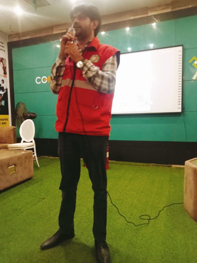 A man in a red Jacket stands in front of a screen, presenting first aid techniques at RJ Mall's orientation session